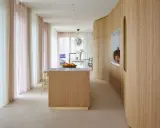 Interno moderno con isola cucina in legno e boiserie curvilinea. Tende leggere color pastello creano un'atmosfera soffusa.