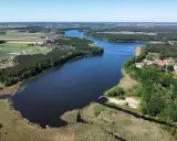 Malownicze jezioro wojnowskie otoczone lasami i polami. W oddali widać zabudowania wsi.