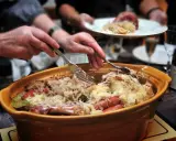 Un plat généreux de choucroute garnie, spécialité de la gastronomie alsacienne, est servi. Des mains servent ce délice, promesse d'une savoureuse nourriture d'Alsace.