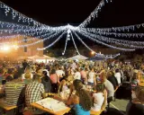 Festa notturna con migliaia di persone sedute ai tavoli, illuminate da festose luminarie. Si celebra la sagra te lu purpu, un evento conviviale.