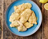 Piatto di pollo al limone su un piatto blu, con limone fresco e rosmarino sullo sfondo.