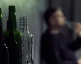 Puste butelki na pierwszym planie, w tle niewyraźna postać pijąca alkohol. Gdzie jest bezpieczna ilość alkoholu?