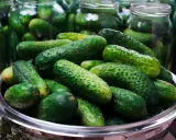 Frische Gurken in einem Metallbehälter, bereit für das Gurken einlegen Rezept. Im Hintergrund stehen viele Einmachgläser.