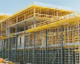 Edificio en construcción con intrincadas estructuras temporales amarillas y grises, sosteniendo los pisos de concreto.