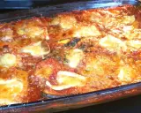 Parmigiana di melanzane appena sfornata, dorata e filante, in una teglia di vetro.
