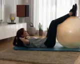 Kobieta wykonuje ćwiczenia na kolana z piłką gimnastyczną w domu.