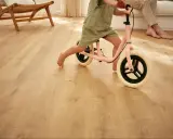 Un enfant apprend à faire du vélo d'équilibre sur un sol de salle de jeux en bois clair.