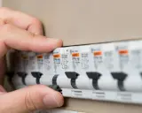Main d'une personne actionnant un disjoncteur dans un tableau électrique. Les plombs ont sauté, il faut rétablir le courant.