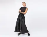 Elegancka kobieta w czarnych, szerokich spodniach i topie z siateczkowymi rękawami. Stylowe, lakierowane mokasyny to idealne buty do teatru.
