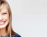 Uśmiechnięta blondynka z niebieskimi oczami, pokazująca, jak obciąć grzywkę na prosto.