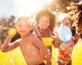 Niños riendo y jugando con globos de agua bajo el sol. Salpicaduras y diversión garantizada en estos juegos acuáticos.