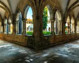 Gotische Arkaden im Kloster Batalha, Portugal. Sonnenschein fällt auf den Steinboden und beleuchtet den grünen Innenhof.