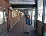 Mujer sonriente saluda bajo el cartel "Welcome to Helsinki". ¡Una aventura en Helsinki con niños comienza!