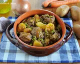 Un saporito spezzatino con patate e piselli, servito in una ciotola di terracotta, con ingredienti freschi sullo sfondo.