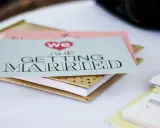 Zaproszenia ślubne "We are getting married" w formacie B0, ułożone na złotym notesie.