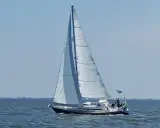 Voilier blanc et bleu naviguant sur une mer calme sous un ciel clair. Les voiles sont gonflées par le vent. Les premiers 375 avis sur ce type de bateau sont positifs.