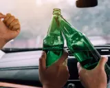 Dwie osoby w samochodzie wznoszą toast zielonymi butelkami piwa 0 5 procent.
