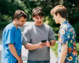 Trzech studentów dyskutuje, czy na studiach są wakacje. Jeden z nich pokazuje coś na telefonie.