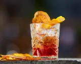 Klasyczny whisky old fashioned w kryształowej szklance, ozdobiony skórką pomarańczy i suszonym owocem.