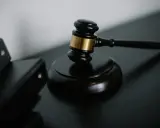 Młotek sędziowski na czarnym tle, obok czarnych segregatorów.