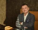 Uśmiechnięty mężczyzna, January Ciszewski, w eleganckiej marynarce siedzi w fotelu.
