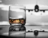 Szklanka whisky z lodem na tle samolotu w locie.