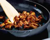 Pfifferlinge braten in einer Pfanne mit einem Holzspatel. Die Pilze sind goldbraun und glänzen in einer köstlichen Sauce.