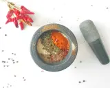 Mortier en pierre rempli d'épices pour fajitas, avec des piments rouges séchés et des grains de poivre à proximité.