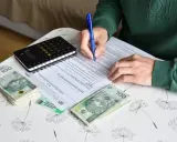 Osoba wypełnia dokumenty dotyczące umowy zlecenia i ubezpieczenia, obok leżą pieniądze i kalkulator.