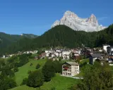 Villaggio alpino con case in pietra e legno, circondato da boschi e verdi pascoli, sotto un'imponente cima rocciosa. Il rifugio Venezia è un luogo incantevole.