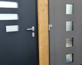 Dwie nowoczesne drzwi wejściowe, jedna ciemnoszara z prostokątnymi przeszkleniami, druga szara z kwadratowymi. Dowiedz się, jak uszczelnić drzwi wejściowe.