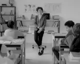 Lehrerin lächelt in einem Klassenzimmer, während Schüler an ihren Tischen sitzen. Eine Szene, die eine gute Klassengemeinschaft widerspiegelt.