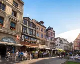 Terrasses animées devant les maisons à colombages de l'incontournable Rouen, sous un ciel bleu éclatant.
