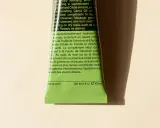 Tubo verde brillante di Aesop con testo in inglese e francese. Il testo descrive un balsamo corpo idratante, spiegando il suo inci significato e gli ingredienti chiave.