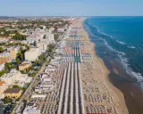 Vista aerea delle frazioni di Rimini: una lunga spiaggia attrezzata con file ordinate di ombrelloni e lettini, hotel e palazzi affacciati sul mare Adriatico.