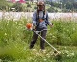 Persona con equipo de protección usa desbrozadora para cortar hierba alta, mostrando la diferencia entre desbrozadora y cortabordes en un paisaje rural.