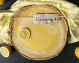 Ein hausgemachter Zitronenkuchen mit einem Zitronenschnitz und einem "Homemade"-Etikett, umgeben von gelben Tüchern und Zitronen.