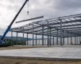 Grúa instala viga en estructura metálica de nave industrial. El diseño de naves industriales avanza con la colocación de elementos clave.