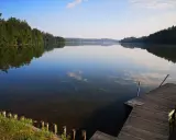 Spokojne jezioro Sulęczyno o poranku. Drewniane molo zaprasza do podziwiania odbijających się w tafli chmur i zielonych lasów.