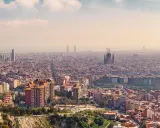 Panorama von Barcelona von oben. Die Sagrada Familia und moderne Wolkenkratzer ragen aus der weitläufigen Stadt hervor.