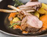 Chuleta de ternasco jugosa, servida sobre puré de zanahoria y patatas asadas, decorada con romero y tomillo.