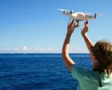 Frau hält Drohne über dem Meer in Kroatien, bereit zum Fliegen.
