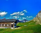 Rifugio Passo San Nicolò, un'accogliente baita in legno con vista su maestose cime innevate e un cielo azzurro brillante.