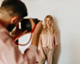 Fotograf robi zdjęcie uśmiechniętej blondynce. Zastanawiasz się, ile kosztuje sesja u fotografa?