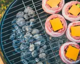 Fem baconsnurrade köttfärsbiffar med ost på en grill för indirekt grillning.