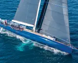 Un grand voilier bleu glisse sur l'eau, tel un tapis volant bateau. L'équipage est à bord, profitant de la navigation.