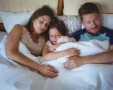 Familia durmiendo junta, la niña abraza un peluche. Un momento de paz que evoca la regresión infantil y la seguridad del hogar.