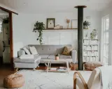 Przytulny salon w stylu skandynawskim nowoczesnym. Szara kanapa, drewniany stolik, regał z książkami i mnóstwo zieleni tworzą relaksującą atmosferę.