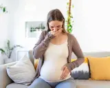 Donna incinta con nausea nel terzo trimestre, copre la bocca con la mano.