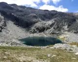 Ein tiefblauer Bergsee in der Sierra de Gredos, umgeben von felsigen Hängen und grünen Wiesen.